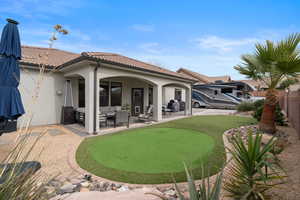 Rear view of house with an area to practice putting, stucco siding, a patio, and a tile roof