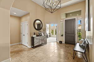 Foyer entrance with stone tile flooring, suspended lighting, and a high ceiling