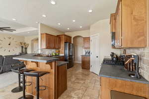 Kitchen featuring dark countertops, arched walkways, a kitchen bar, open floor plan, and a textured ceiling