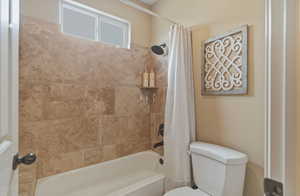 Bathroom featuring toilet and shower / bathtub combination with curtain