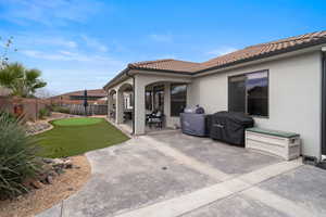 Rear view of house with a patio, stucco siding, a fenced backyard, a tiled roof, and a putting green