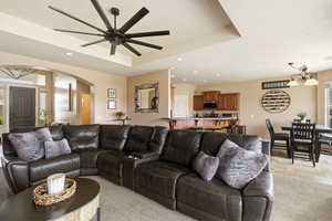 Living room featuring a ceiling fan, hanging lights, arched walkways, light stone finish flooring, and a tray ceiling