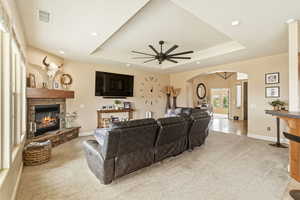 Living room featuring a tray ceiling, light carpet, a fireplace, recessed lighting, and arched walkways