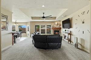 Living room with a stone fireplace, a ceiling fan, carpet flooring, recessed lighting, and a raised ceiling
