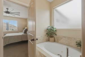 Ensuite bathroom featuring a whirlpool tub, carpet floors, and ceiling fan
