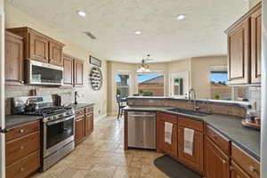 Kitchen with stainless steel appliances, a peninsula, stone tile floors, and wood finish cabinetry