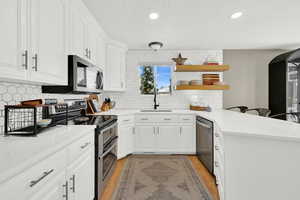 Kitchen with a peninsula, stainless steel appliances, light wood-type flooring, white cabinets, and open shelves