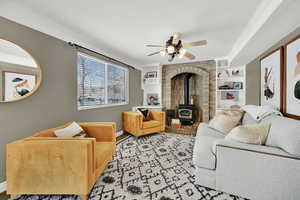 Living room with a wood stove, built in shelves, ceiling fan, crown molding, and a textured ceiling