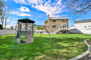 Rear view of house with a fenced backyard, a playground, a chimney, and a wooden deck