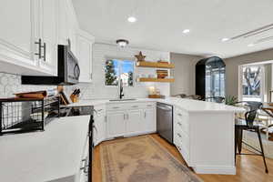 Kitchen featuring a peninsula, white cabinets, light wood finished floors, open shelves, and light stone countertops