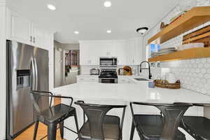Kitchen with stainless steel appliances, a peninsula, light stone countertops, decorative backsplash, and a kitchen breakfast bar