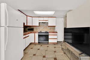 Two tone kitchen featuring two tone cabinets, freestanding refrigerator, range with electric stovetop, stone tile flooring, and backsplash