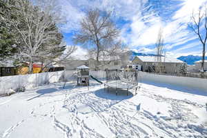 Yard layered in snow featuring a trampoline, a fenced backyard, a mountain view, and a playground