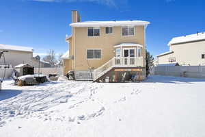 Snow covered house featuring a fenced backyard, a deck, and a chimney