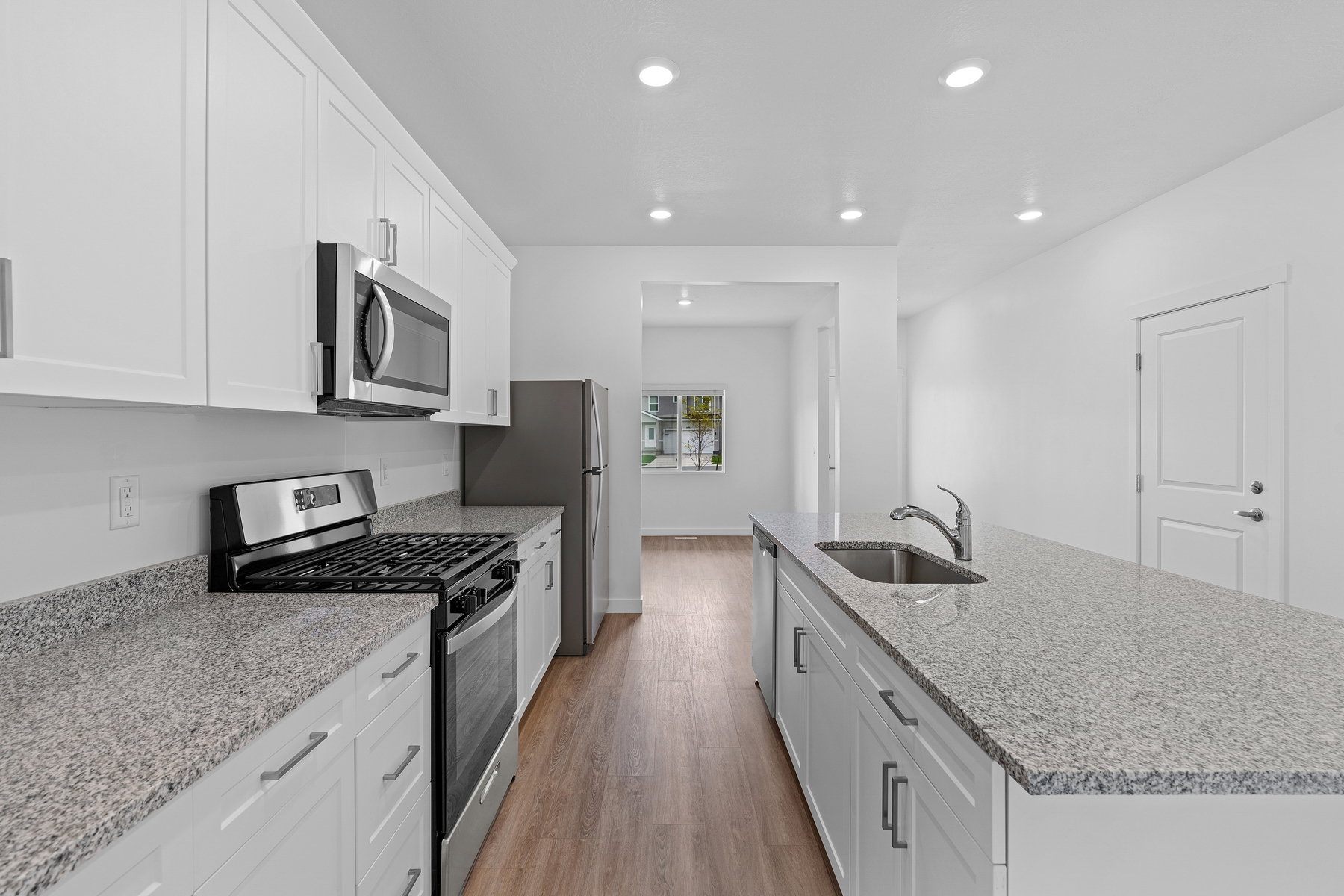 Kitchen with stainless steel appliances, a center island with sink, light stone counters, white cabinets, and light wood-style flooring