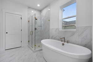 Full bathroom featuring a marble finish shower, marble look tile flooring, recessed lighting, a soaking tub, and tile walls