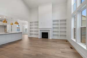 Unfurnished living room featuring a high ceiling, a fireplace, dark wood-type flooring, hanging lights, and built in shelves