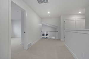 Corridor with vaulted ceiling, light colored carpet, and recessed lighting
