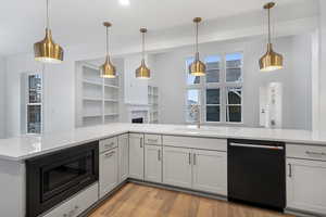 Kitchen with pendant lighting, light stone counters, black appliances, light wood-style floors, and a fireplace