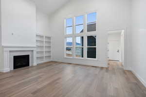 Unfurnished living room with a fireplace, a mountain view, lofted ceiling, and light wood-type flooring