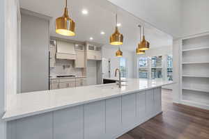 Kitchen featuring glass insert cabinets, light stone counters, decorative light fixtures, dark wood-style floors, and white cabinetry