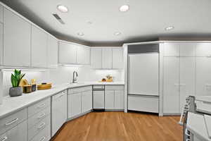 Kitchen with light countertops, built in refrigerator, light wood-type flooring, white dishwasher, and recessed lighting
