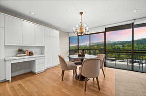 Dining room with built in study area, light wood-style floors, a chandelier, and floor to ceiling windows