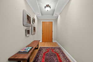 Doorway with wood finished floors, crown molding, and a raised ceiling