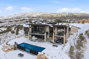 Snow covered house with stone siding, a pool, a patio, and a mountain view