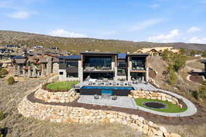 Back of house featuring a balcony, a patio area, stone siding, a mountain view, and an outdoor fire pit