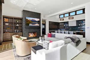 Living area with light wood-style floors, a stone fireplace, a high ceiling, and recessed lighting