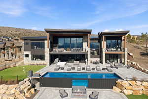 Back of property featuring a balcony, stone siding, a patio area, a mountain view, and an outdoor living space with a fire pit