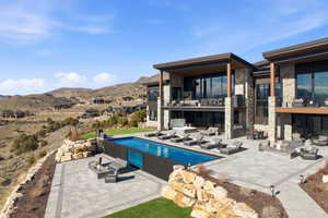 Rear view of house with a balcony, a patio, stone siding, and a mountain view