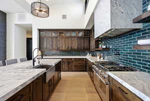 Kitchen featuring dark wood finish cabinets, range with two ovens, backsplash, light stone countertops, and a high ceiling