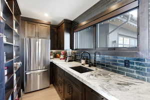 Kitchen with dark wood finish cabinetry, freestanding refrigerator, light stone countertops, and decorative backsplash