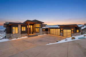 View of front facade with stone siding, driveway, an attached garage, and board and batten siding