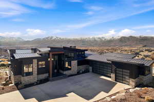 View of front of house with stone siding, a garage, a standing seam roof, and driveway