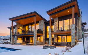 Snow covered rear of property with stone siding, a patio, a balcony, and an outdoor pool