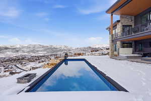 Snow covered pool featuring an outdoor pool, a mountain view, a balcony, and a patio