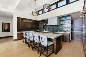 Kitchen featuring dark wood finish cabinetry, a large island, open shelves, a breakfast bar area, and a high ceiling