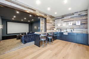 Home theater room with light wood-style floors, recessed lighting, and bar with sink