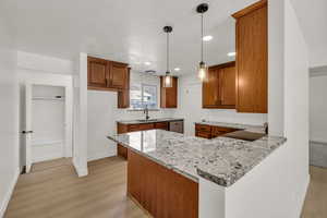 Kitchen featuring wood finish cabinets, a peninsula, light stone counters, pendant lighting, and light wood-style flooring