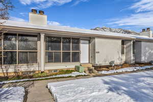 Snow covered house featuring a chimney, stucco siding, and entry steps