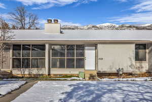 Snow covered back of property with entry steps, a chimney, and a mountain view