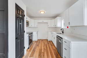 Kitchen with white cabinets, stainless steel appliances, light wood finished floors, light stone countertops, and decorative backsplash