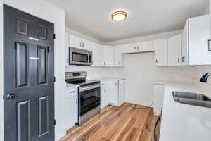 Kitchen featuring stainless steel appliances, white cabinetry, light wood-style flooring, and tasteful backsplash