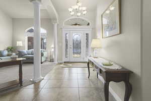 Tiled entrance foyer featuring decorative columns, a chandelier, arched walkways, carpet flooring, and a high ceiling