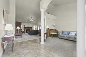 Living area featuring light carpet, decorative columns, a ceiling fan, a warm lit fireplace, and light tile patterned floors