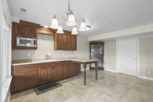 Kitchen featuring light countertops, stainless steel microwave, suspended lighting, wood finish cabinets, and a peninsula