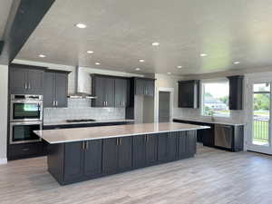 Kitchen with a spacious island, stainless steel appliances, tasteful backsplash, light stone countertops, and light wood-type flooring